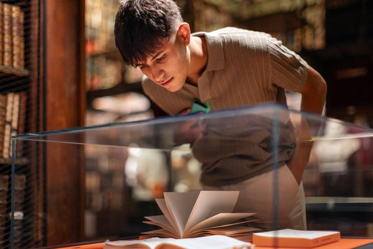 Een jonge man buigt zich over een glazen vitrinekast waarin een bibliofiel boek ligt