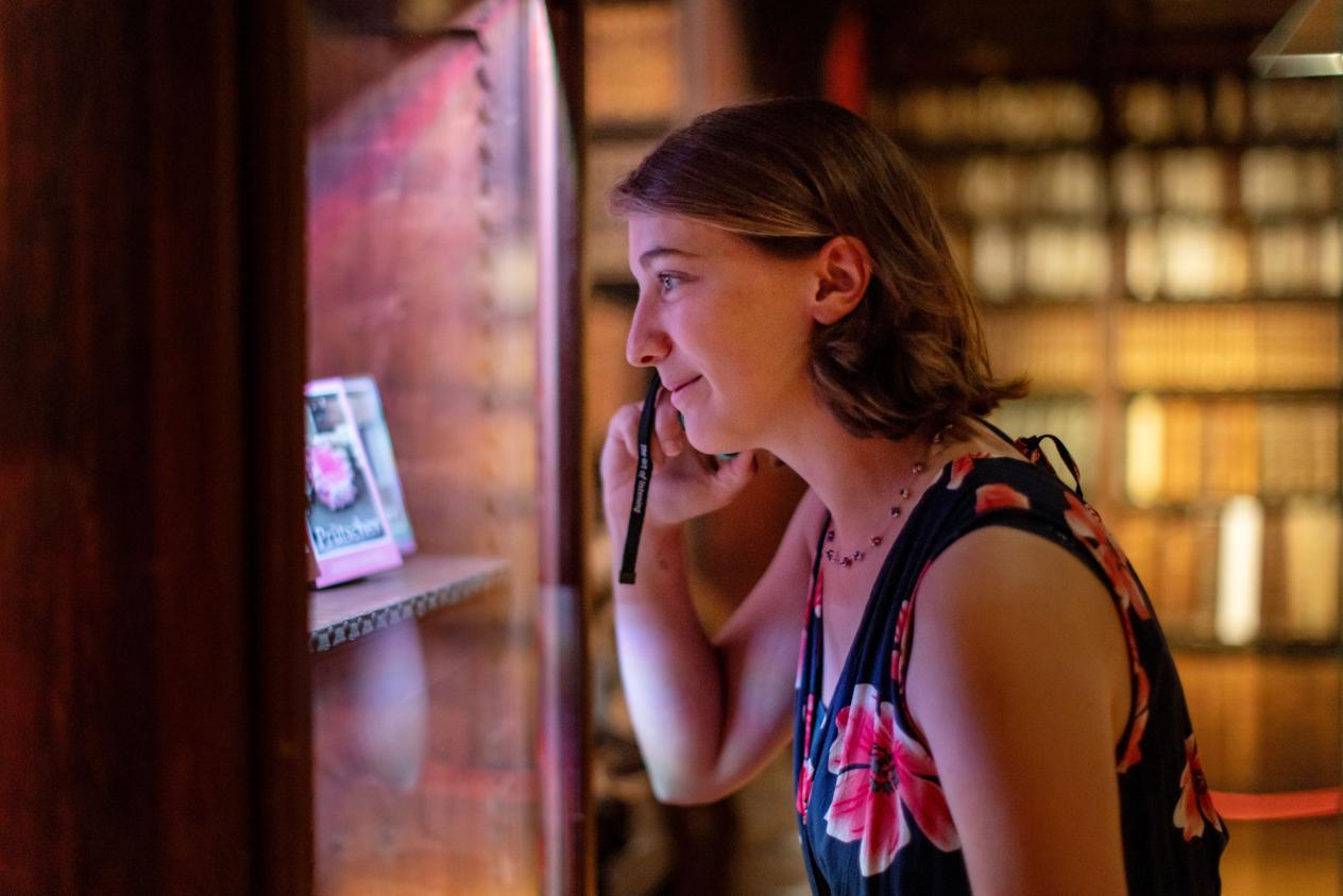 Een vrouw kijkt in de vitrine met de audiogids aan haar oor