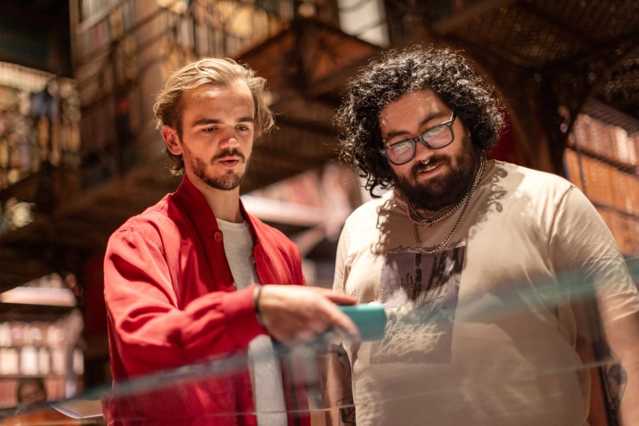 Twee jonge mannen bekijken de expostukken in een vitrinekast en wijzen iets aan