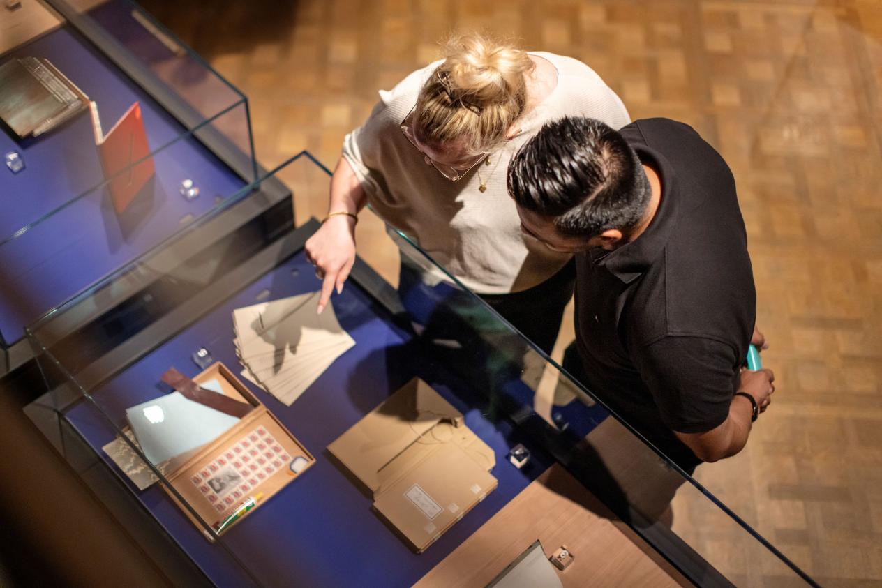 Bovenaanzicht van een man en vrouw die in een glazen kast naar de tentoongestelde bibliofiele uitgaven kijken
