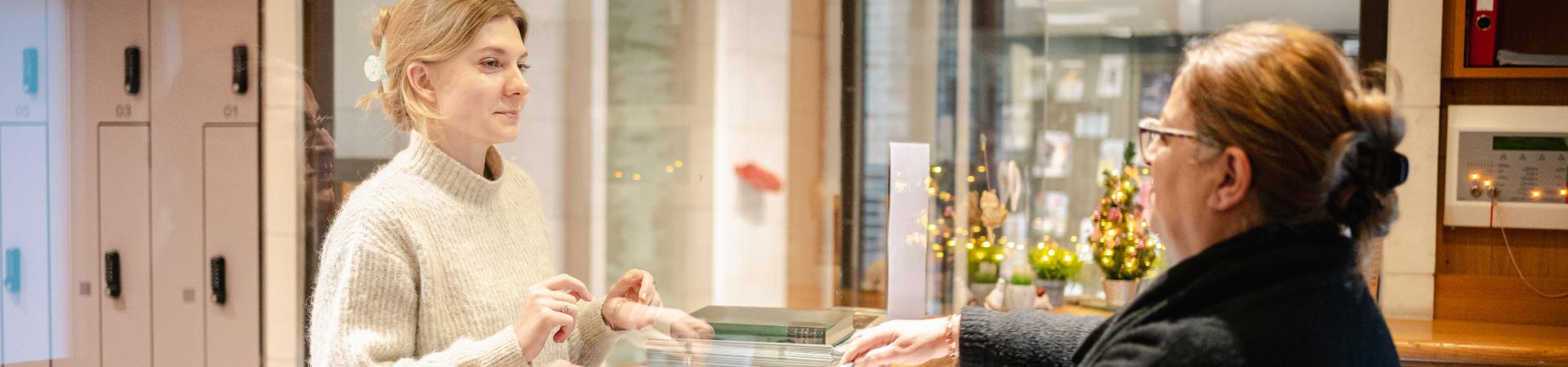 Jonge vrouw meldt zich aan bij medewerker onthaalbalie Erfgoedbibliotheek Hendrik Conscience.