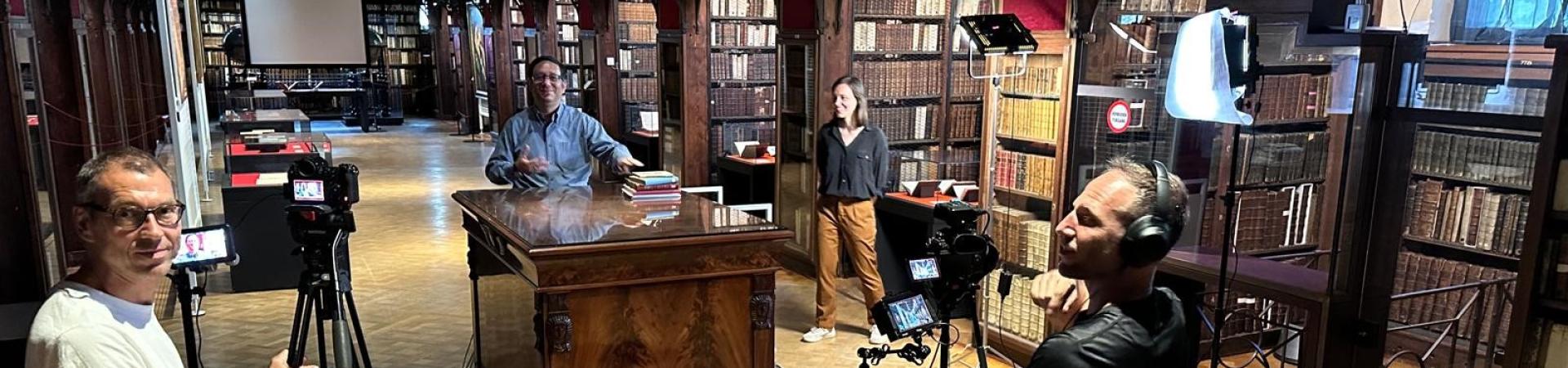 Twee cameramannen met statief maken opnames van een verteller aan Egyptische kast in Nottebohmzaal.