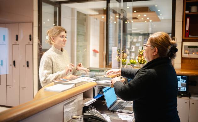 Jonge vrouw meldt zich aan bij medewerker onthaalbalie Erfgoedbibliotheek Hendrik Conscience.